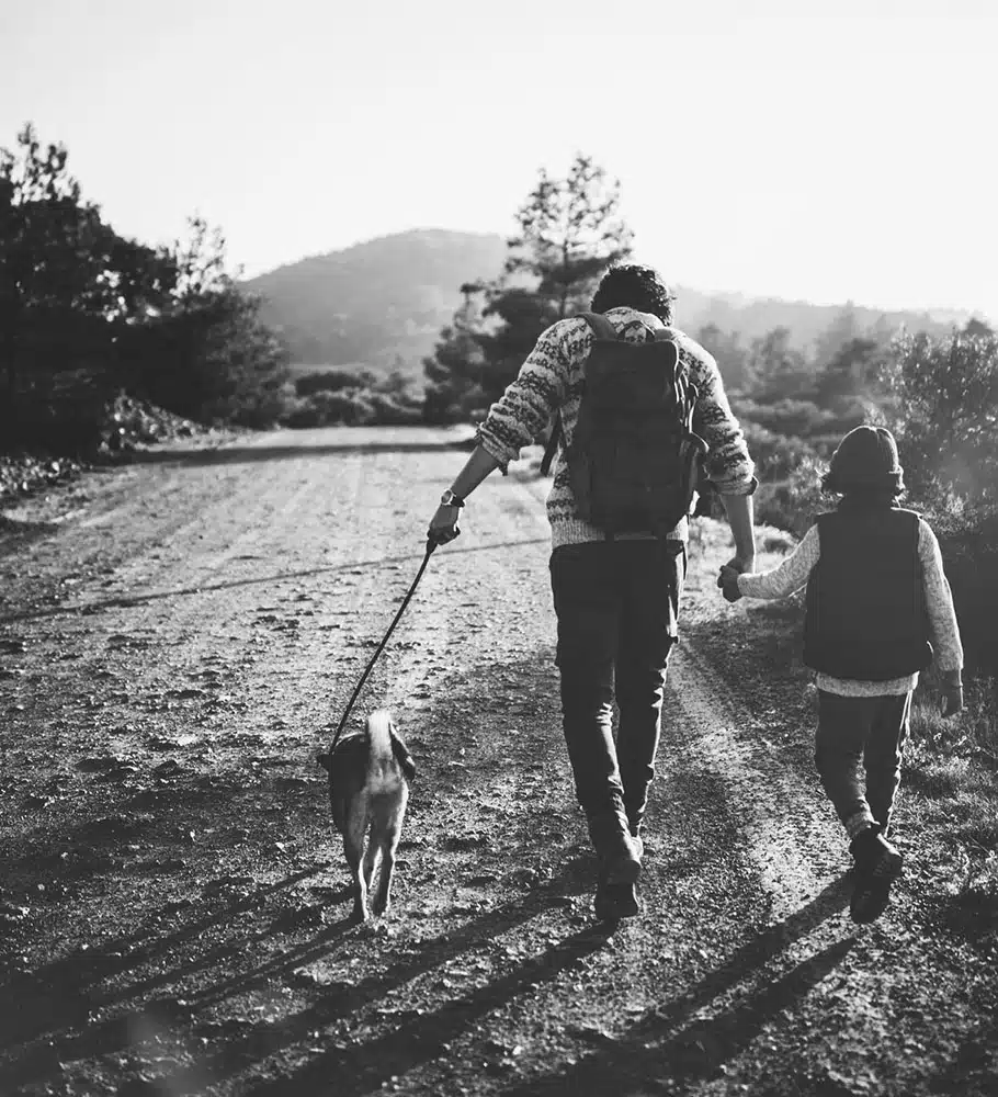 Father and son with pet dog walking on mountain dirt road on camping vacations adventure