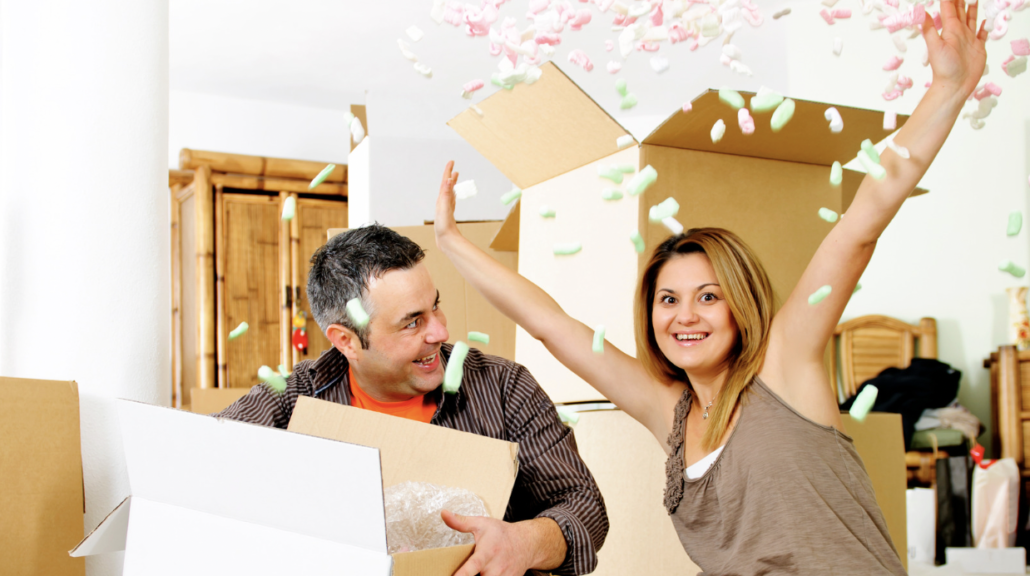 Image of a man and woman moving into a new home, with the woman showering packaging peanuts out of a moving box in a celebratory fashion.