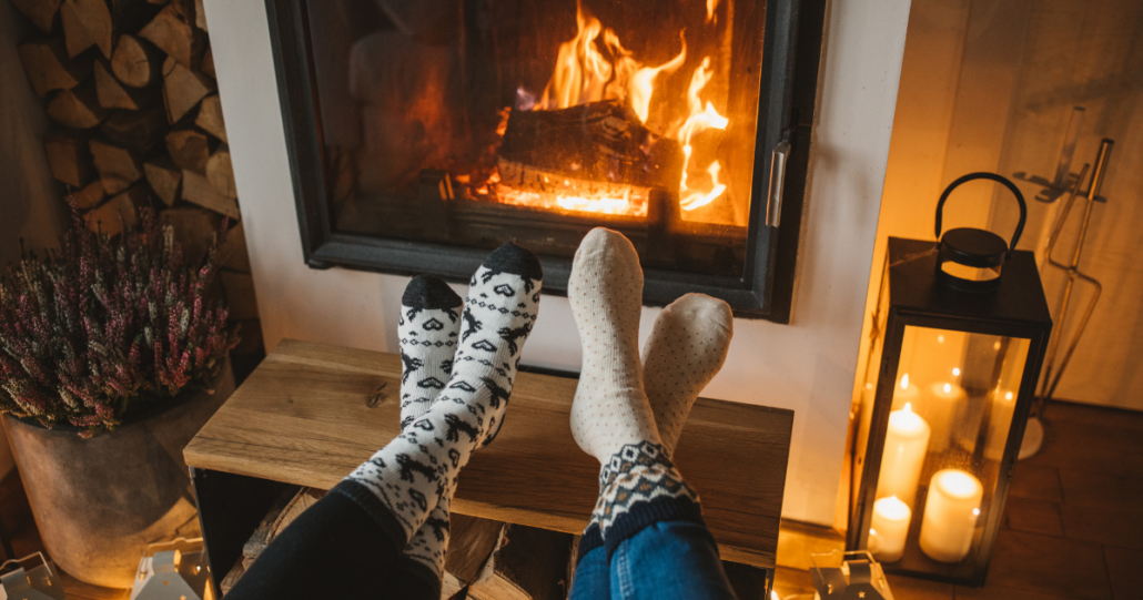 A couple enjoying warm drinks in front of a fireplace during cold months.