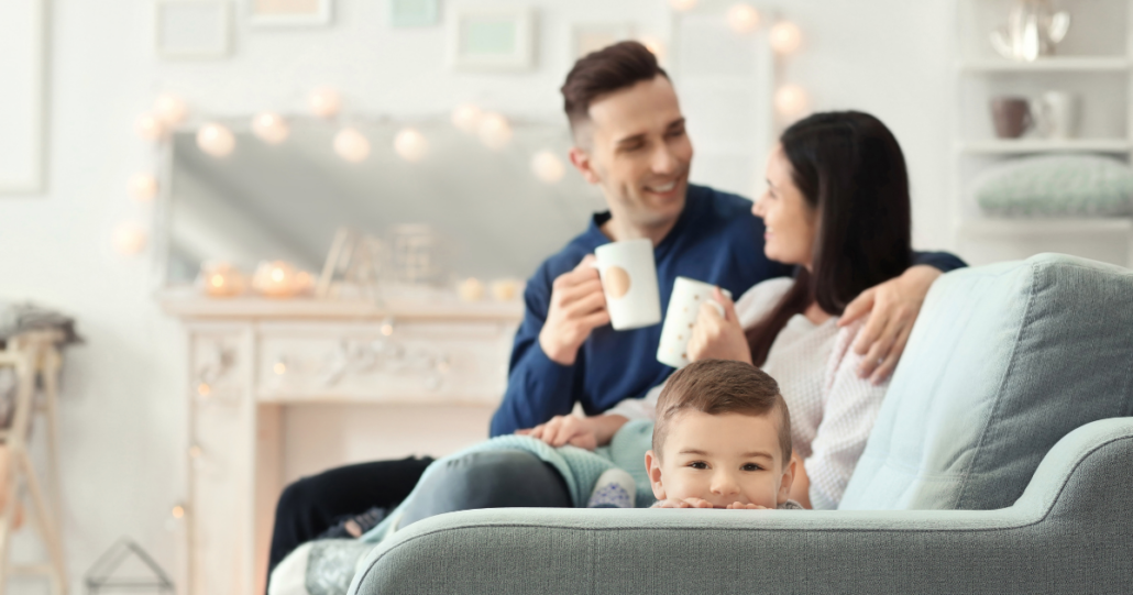 Parents enjoy coffee while sitting on the couch during winter with their son near them.