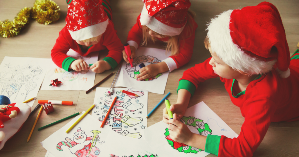 Three kids in Santa hats gathered around their living room, coloring for Christmas.