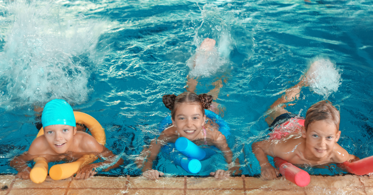 Three kids in an indoor public swimming pool having fun.