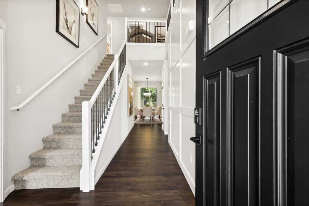 Front entry with white walls, dark flooring and metal railing up a carpeted staircase.