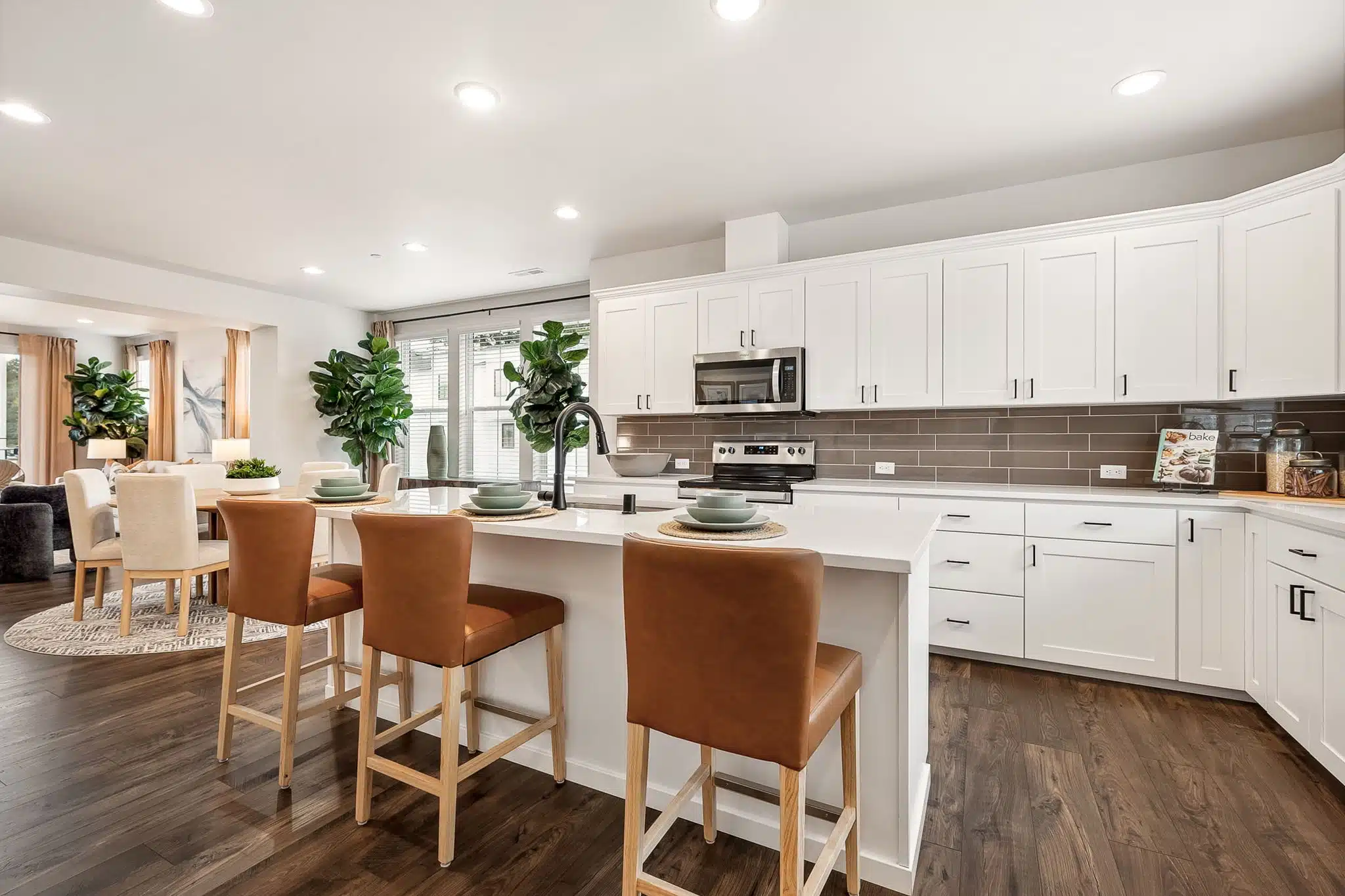Large kitchen island with 4 stools, wood flooring and white cabinetry.