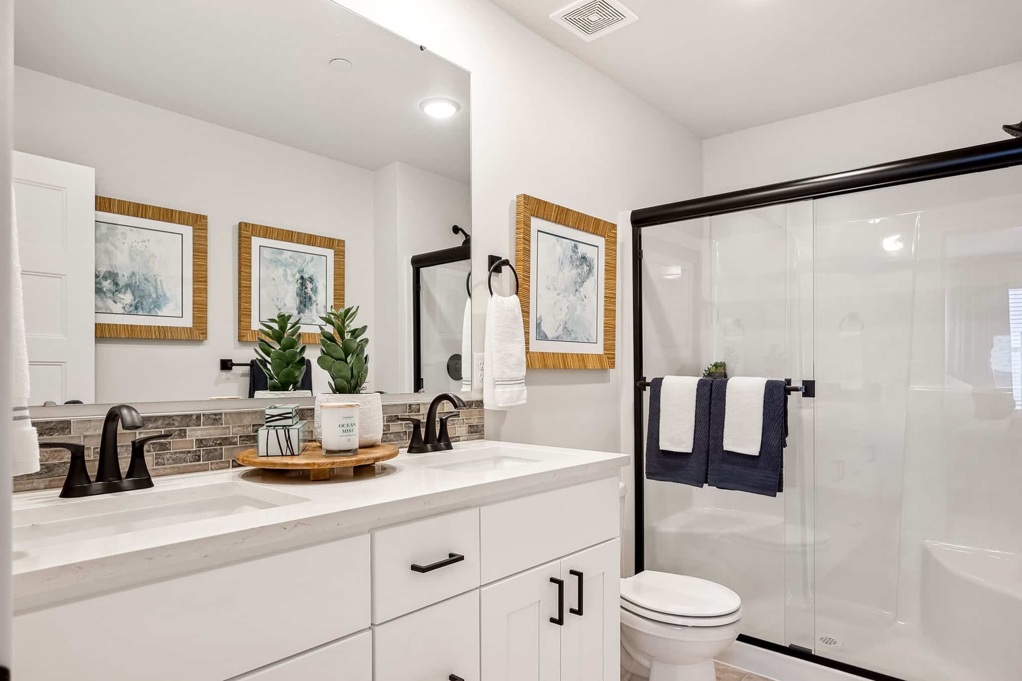 3/4 bath with large mirror, white cabinetry and dark hardware.