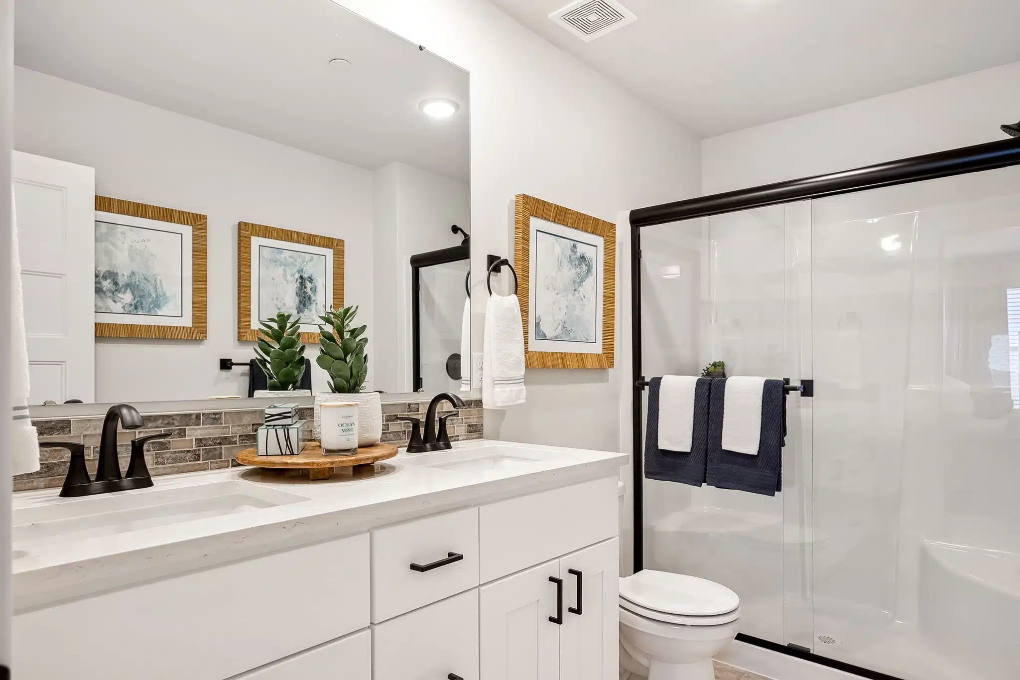 3/4 bath with large mirror, white cabinetry and dark hardware.