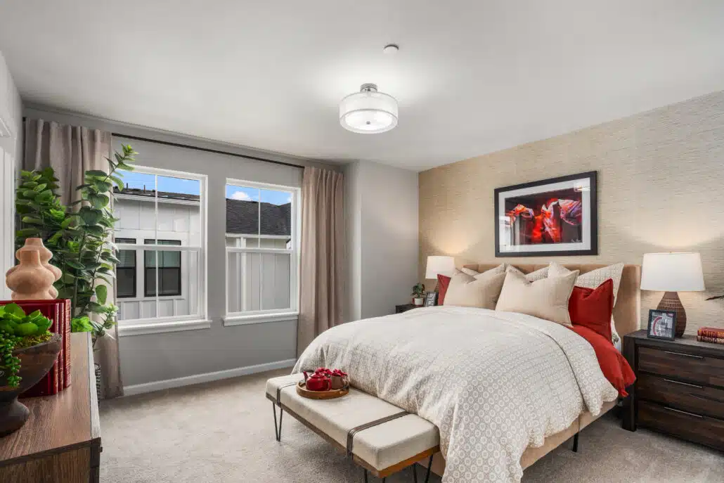 A small bedroom with two windows. There is a bench at the foot of the bed and a photograph of horses on the wall.