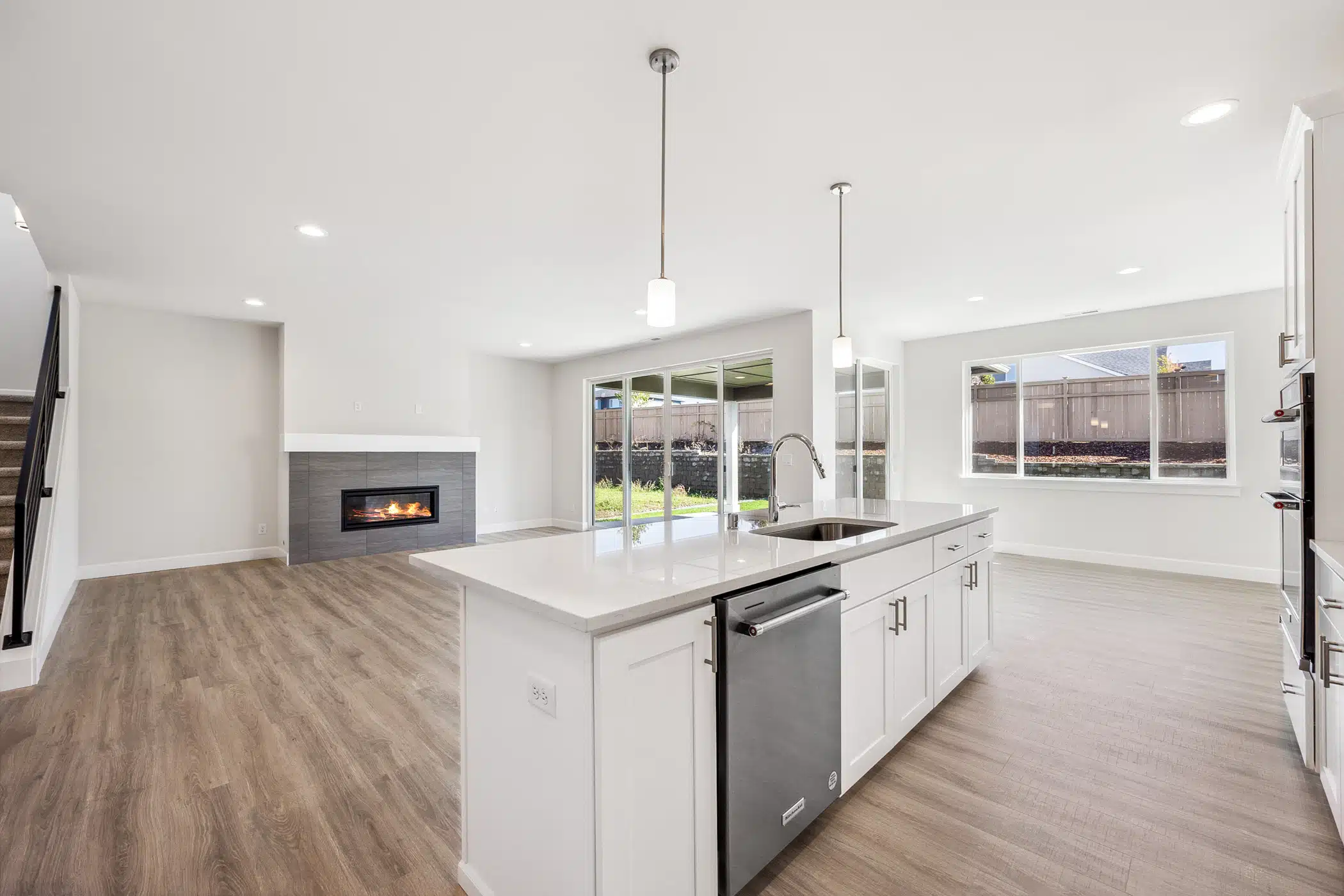 A kitchen island with inset dishwasher and sink. Behind it is an empty living room with a fireplace against the far wall.