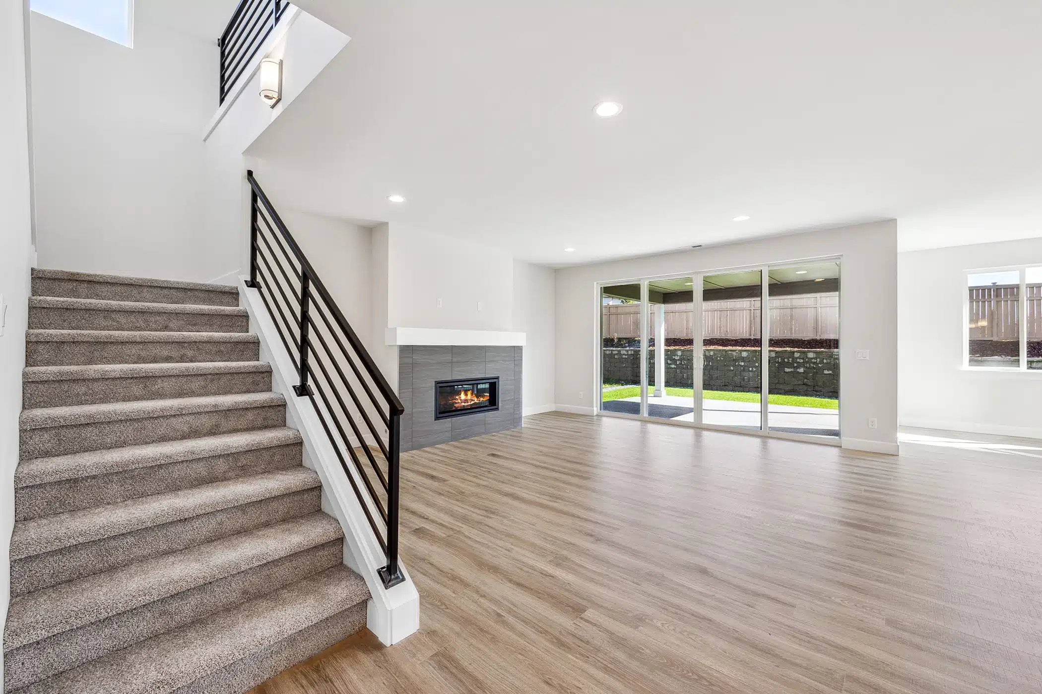 An empty living room with wood floors and a fireplace. A carpeted staircase leads up on the left.