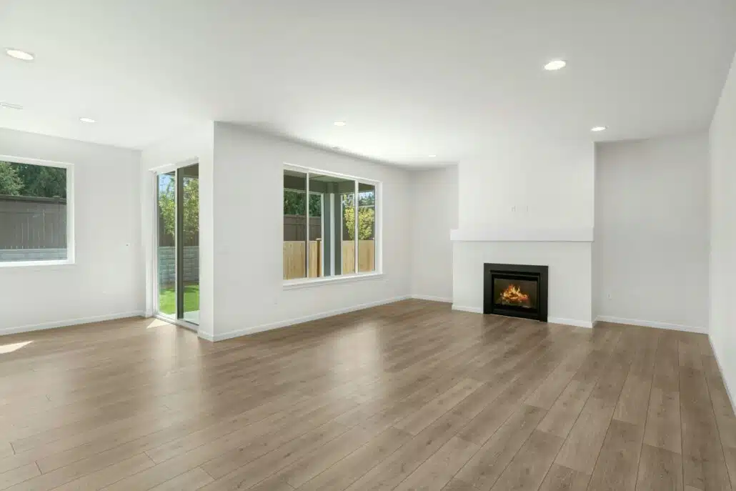 An empty living room with wood floors and a fireplace on the far wall.