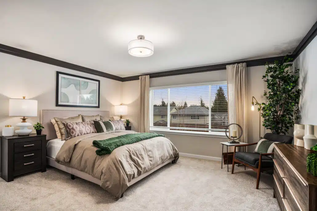 A carpeted bedroom with tan walls, modern wood furniture and a green blanket on the bed.