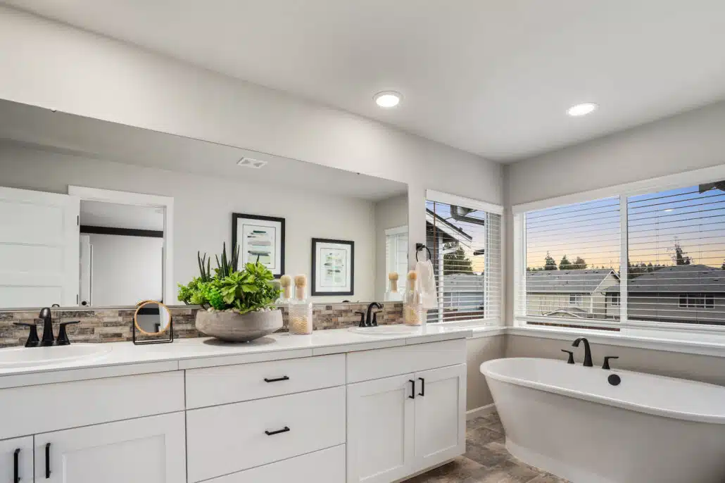 A modern white bathroom with a white tub. Windows overlook a sunset.
