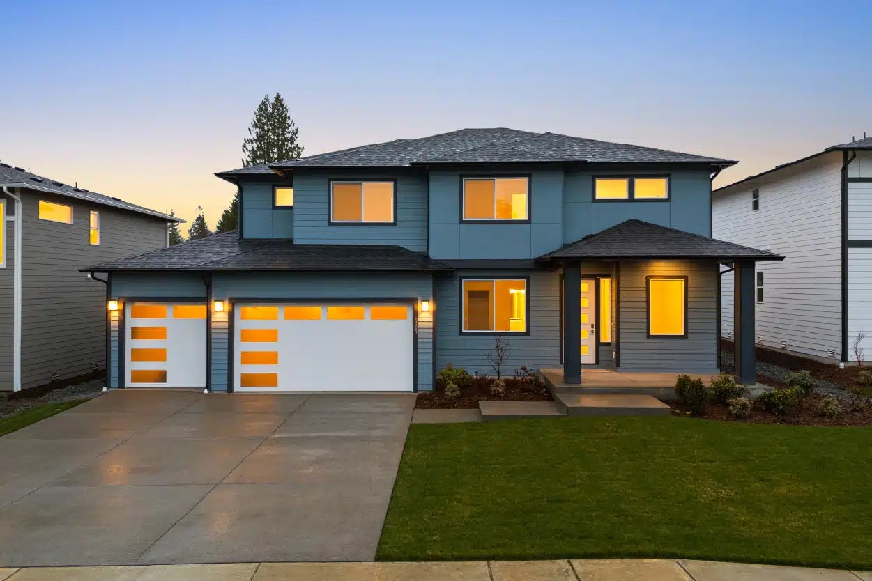 A modern two-story house with blue siding. The windows are lit up with warm lighting.