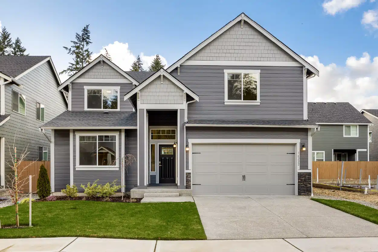A grey, two-story townhouse with white trim under a blue sky.