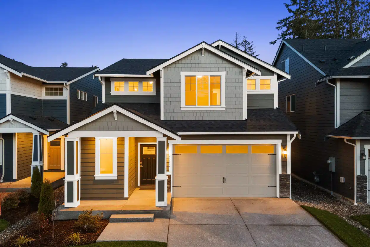 A two-story townhouse with it's lights on under a dusk sky.