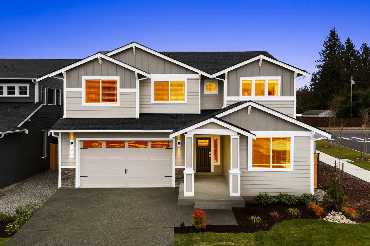 A modern two-story house with warm lighting inside, photographed at dusk.