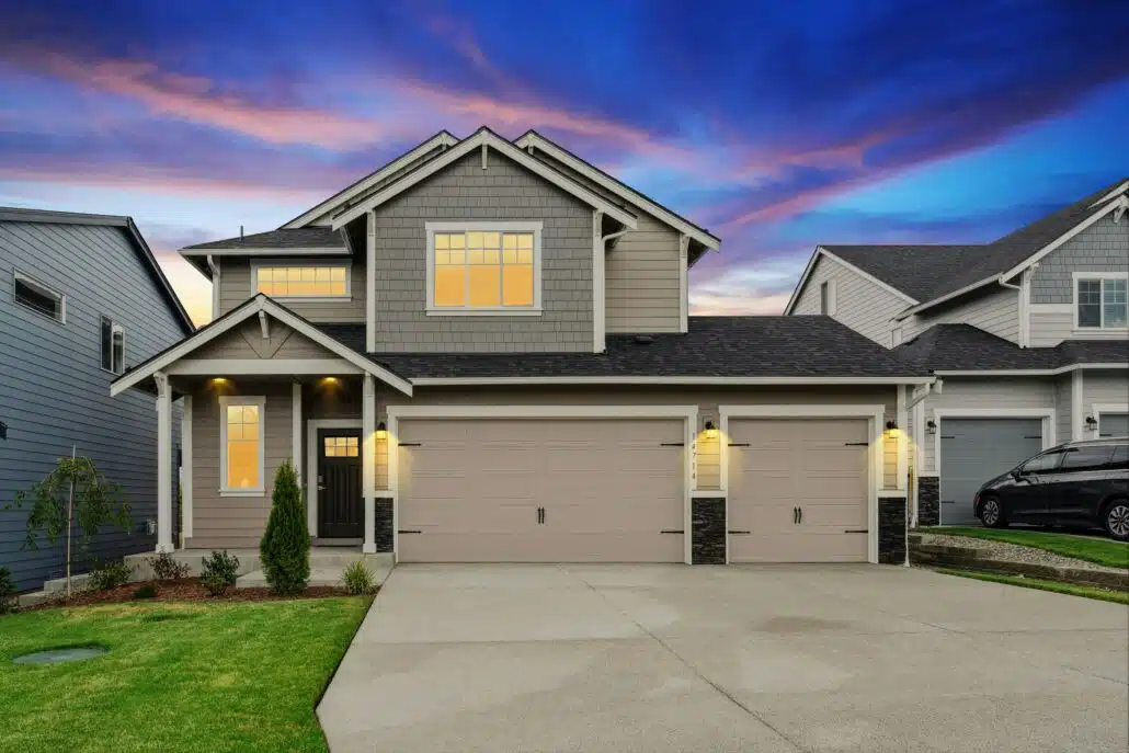 Front of the same two-story house at sunset with porch and garage lights turned on.
