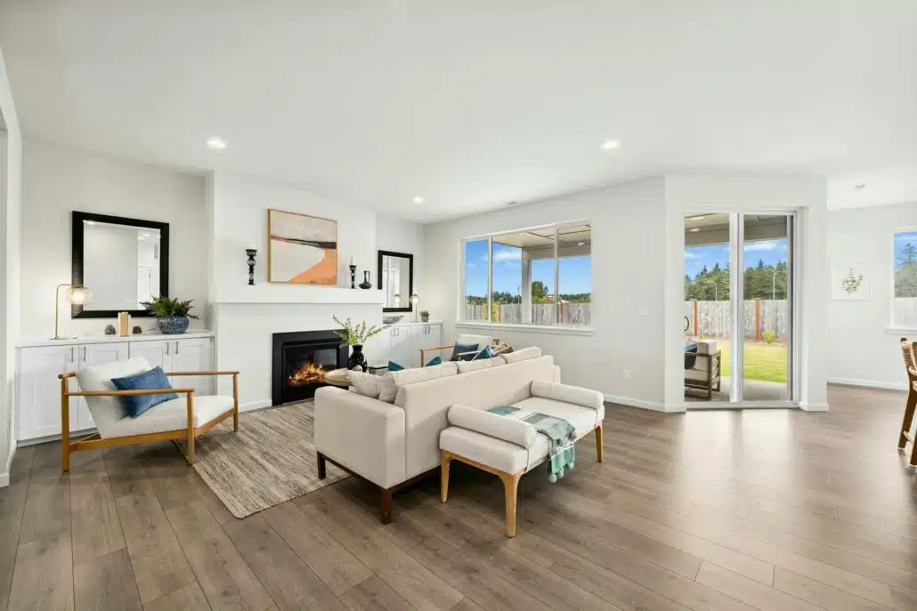 Bright living room featuring a fireplace, white sofa, accent chairs, and windows overlooking the backyard.