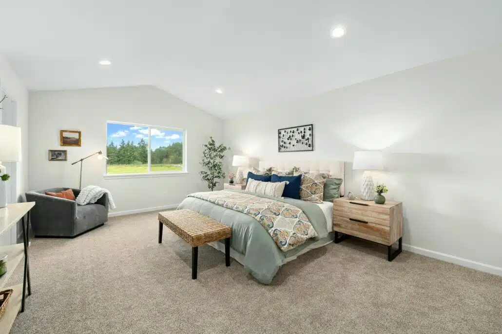Bright bedroom with a large window, upholstered bed, patterned bedding, and a cozy chair in the corner.