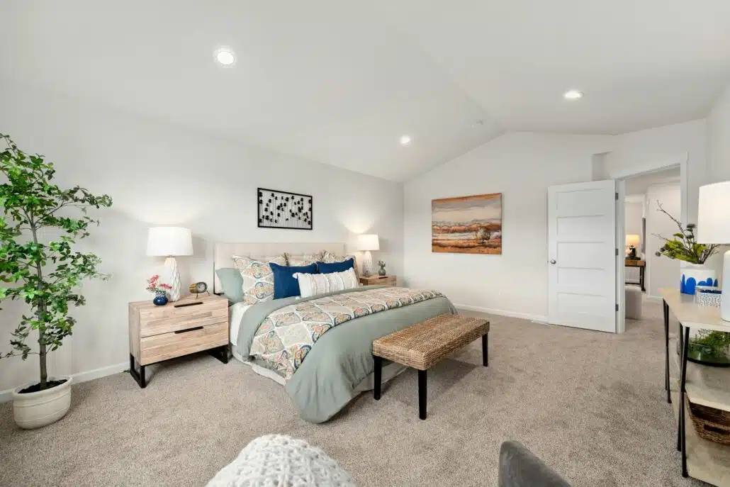Cozy bedroom with a large bed, two nightstands, lamps, wall art, and neutral carpet flooring.