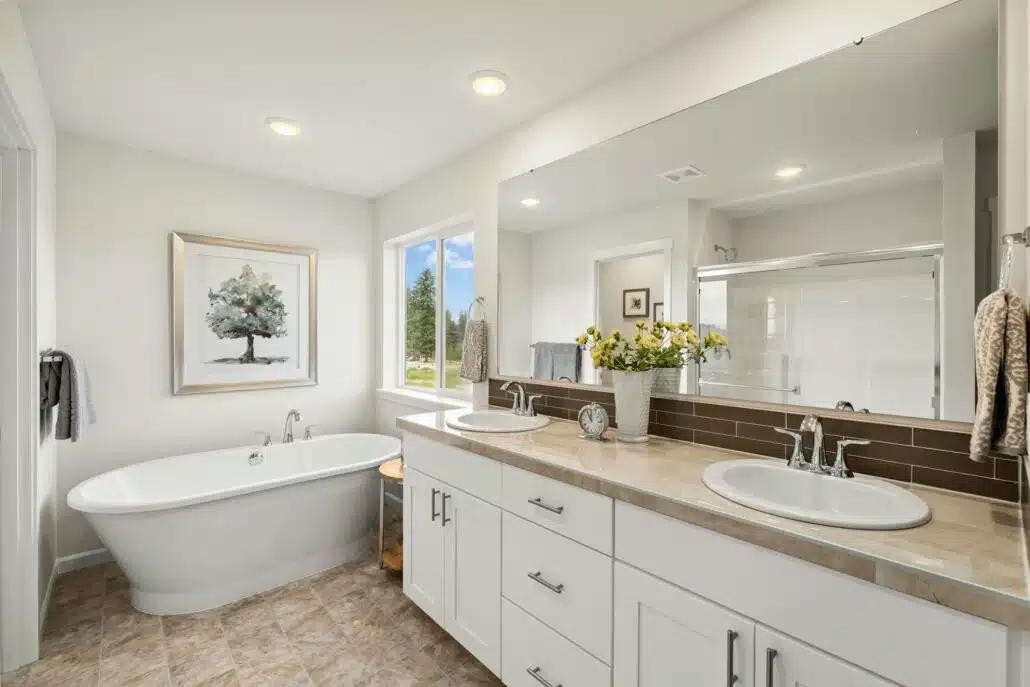 Spacious bathroom featuring a freestanding bathtub, double sinks, large mirror, and natural light from a nearby window.