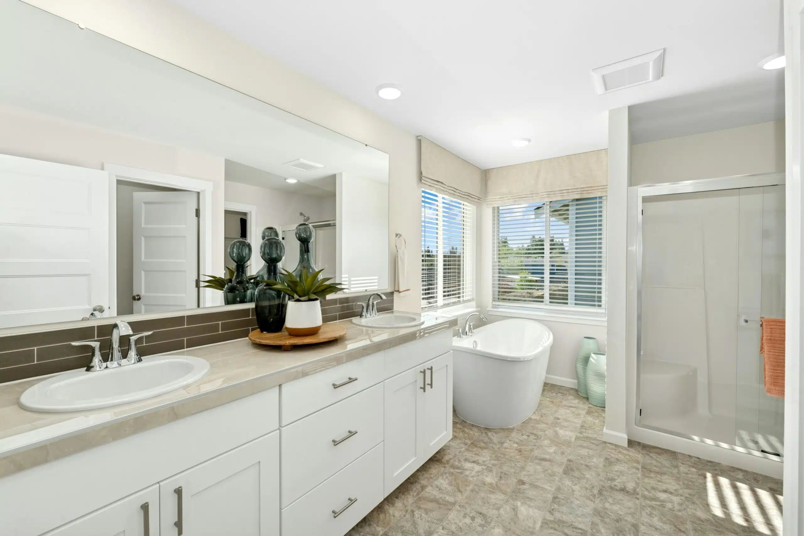 Primary bathroom with dual vanity, bathtub, shower and large corner windows.