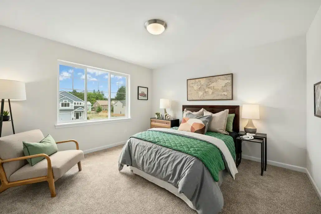 Cozy bedroom with a neatly made bed, accent chair, nightstands, and large window with a view of neighboring homes.